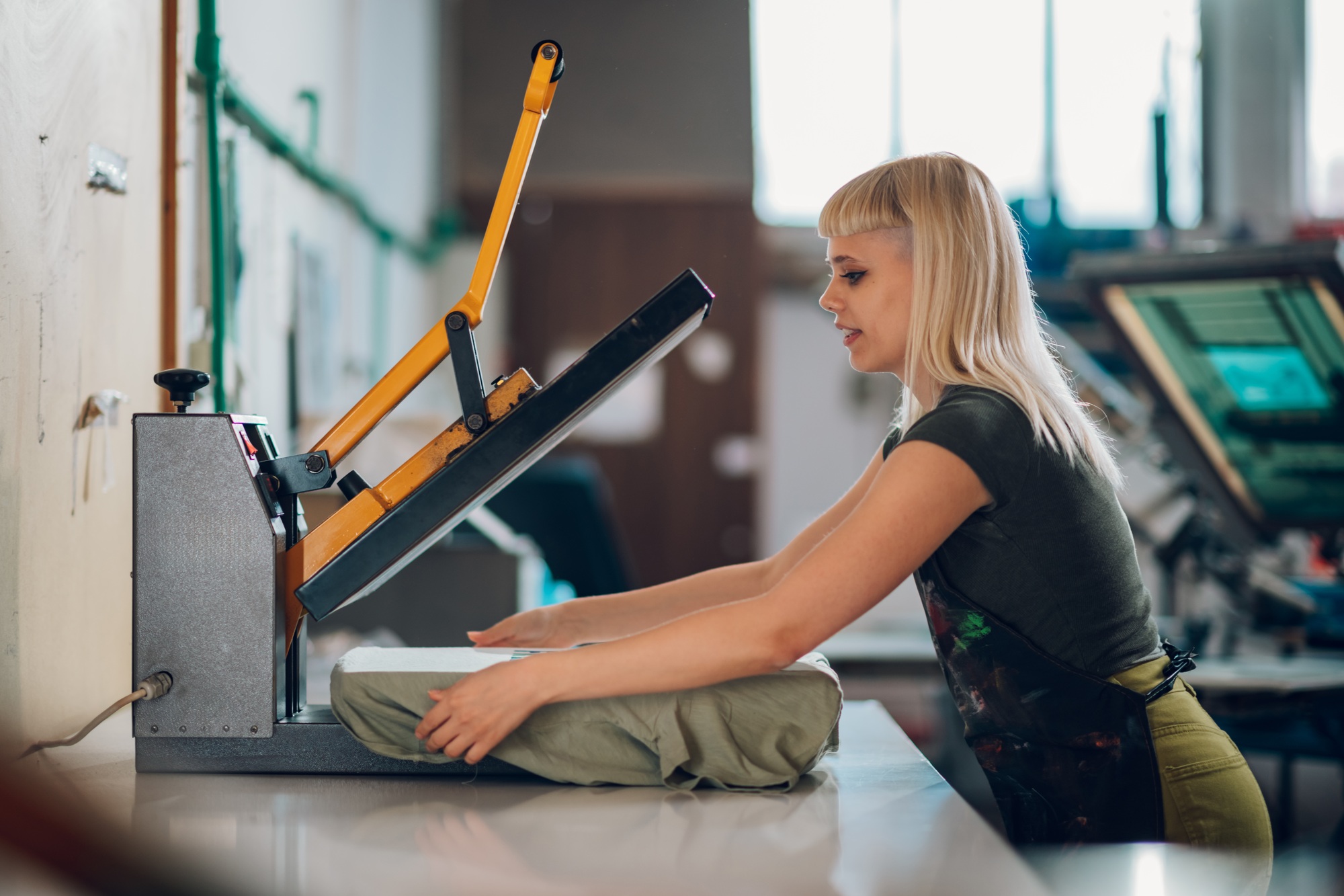 Print shop employee using heating press on screen printed t-shirt.